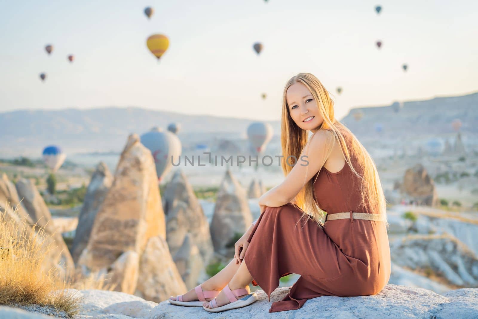 Tourist woman looking at hot air balloons in Cappadocia, Turkey. Happy Travel in Turkey concept. Woman on a mountain top enjoying wonderful view.