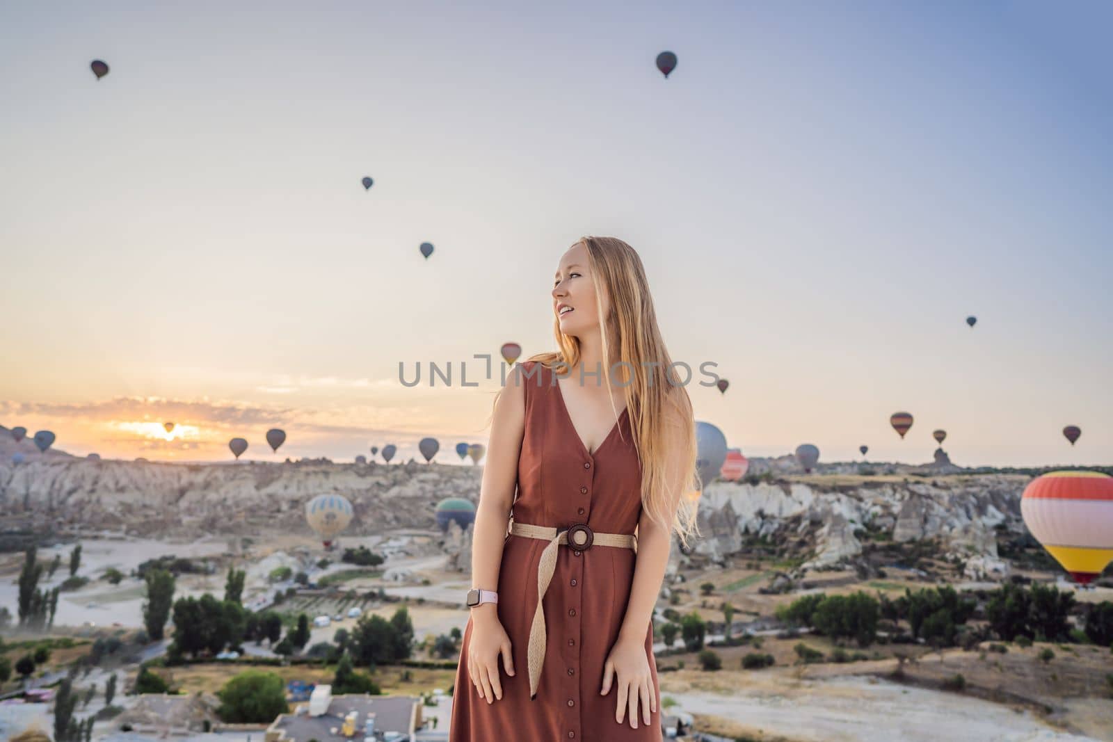 Tourist woman looking at hot air balloons in Cappadocia, Turkey. Happy Travel in Turkey concept. Woman on a mountain top enjoying wonderful view.