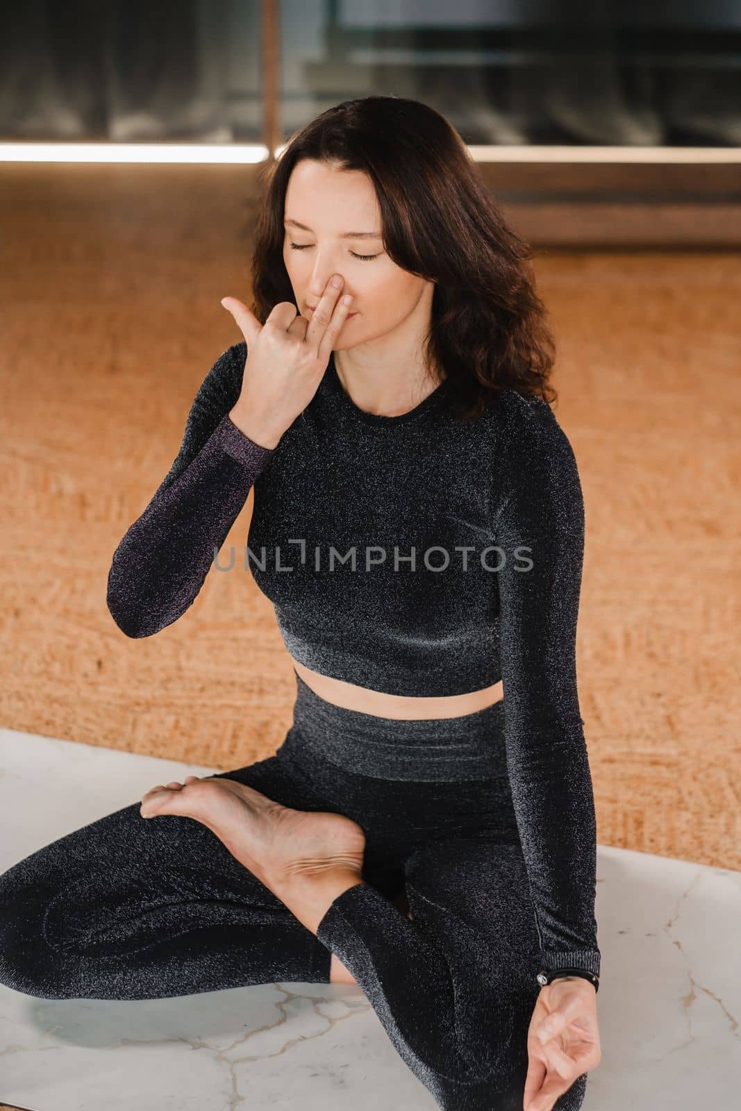A woman in a black tracksuit sits on a yoga mat in a lotus position in the gym by Lobachad