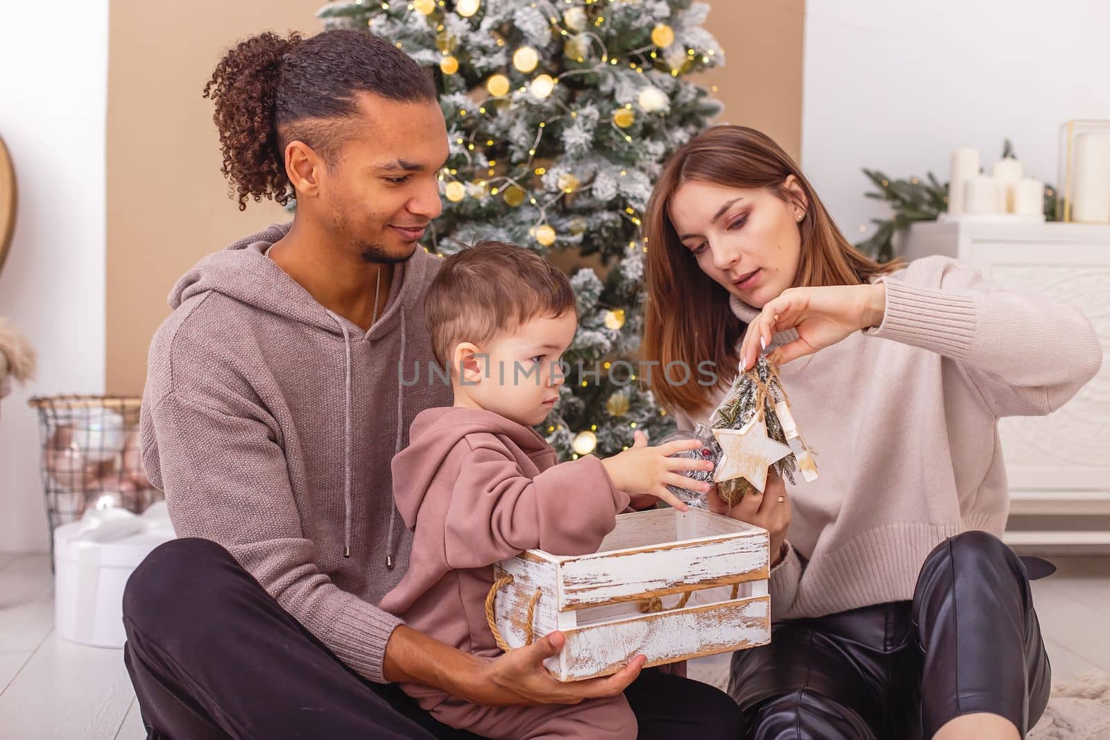 A young multi-racial family with a little boy is sitting on a knitted blanket, holding a wooden Christmas toys. Close up