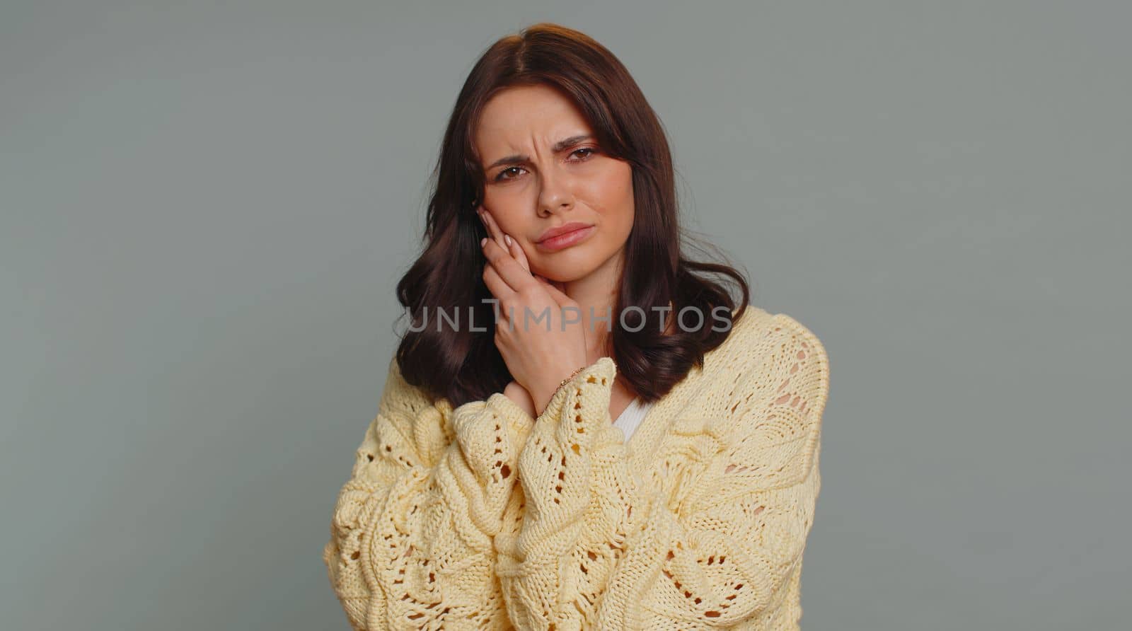 Hipster pretty woman touching sore cheek suffering from toothache cavities or gingivitis waiting for dentist appointment gums disease. Young girl indoor studio shot isolated alone on gray background