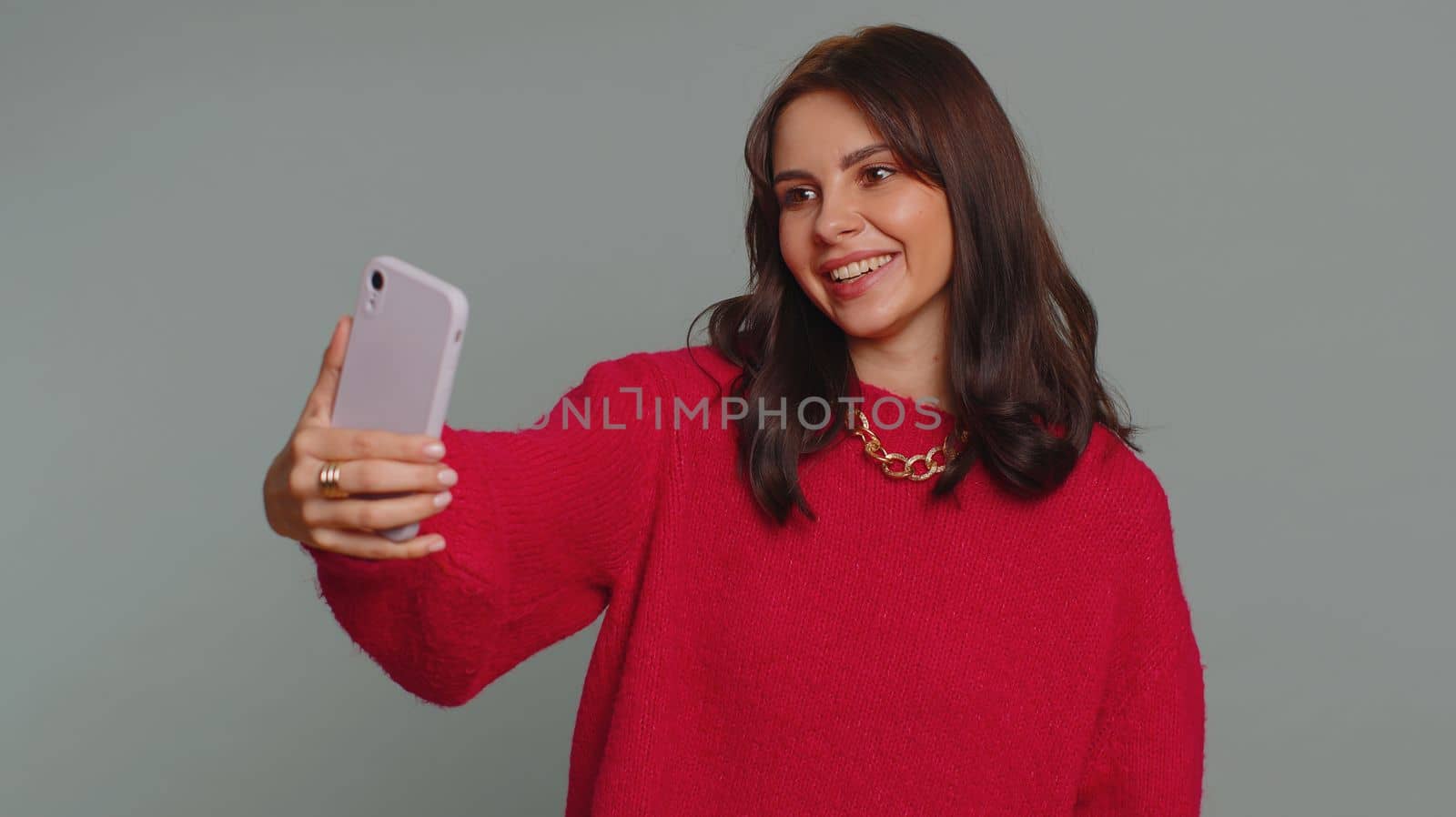 Pretty young woman influencer blogger taking selfie on smartphone, communicating video call online, recording new social media vlog story for subscribers. Girl isolated on gray studio background