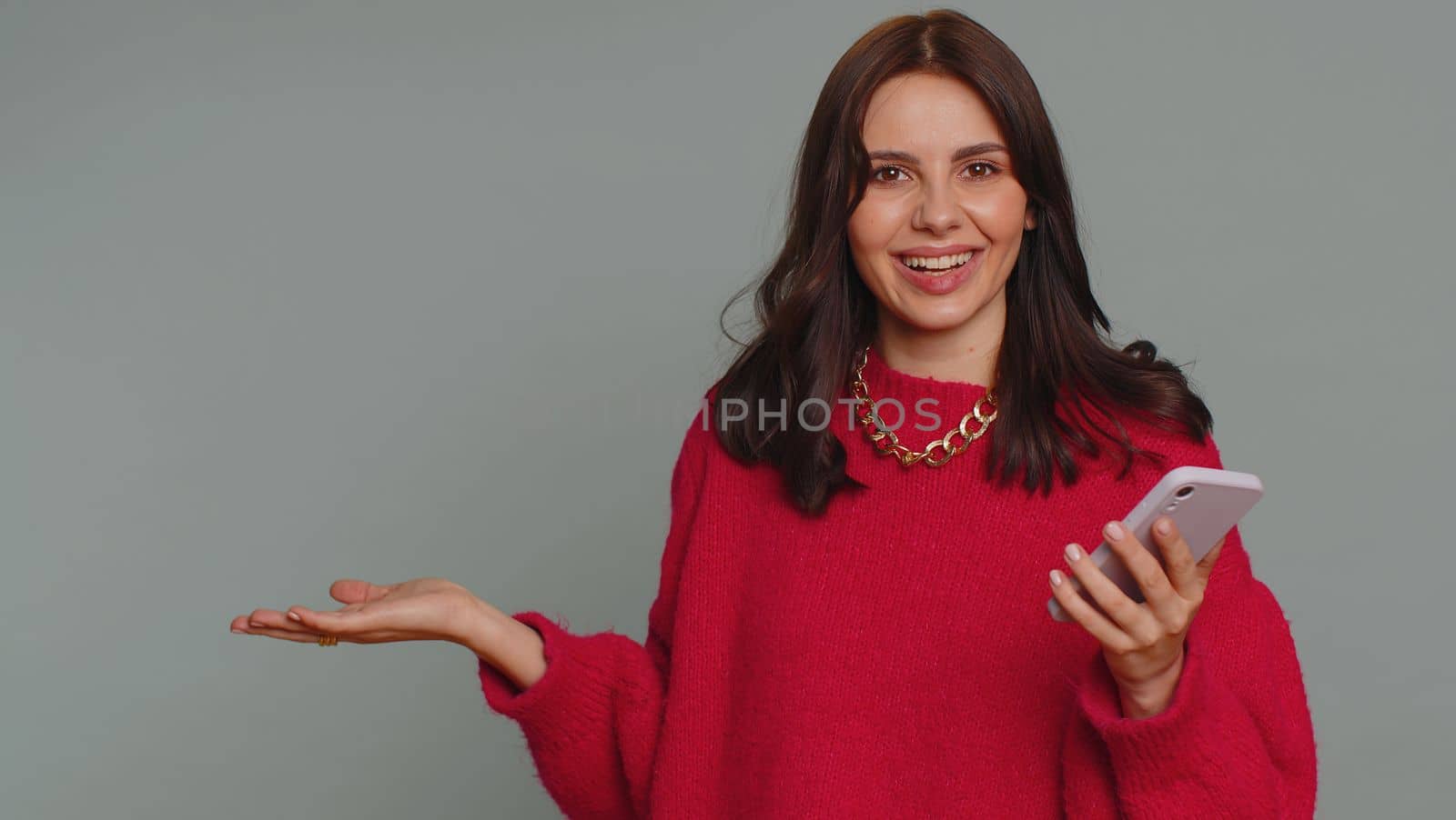 Woman using smartphone pointing empty place, advertising area for commercial text, copy space for goods application promotion social networks positive feedback. Girl isolated on gray studio background