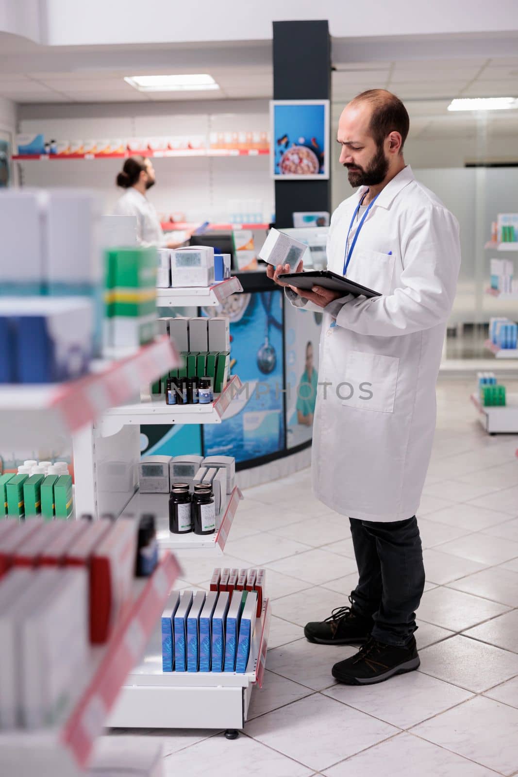 Pharmacist looking at pills packages typing inventory information on tablet computer by DCStudio