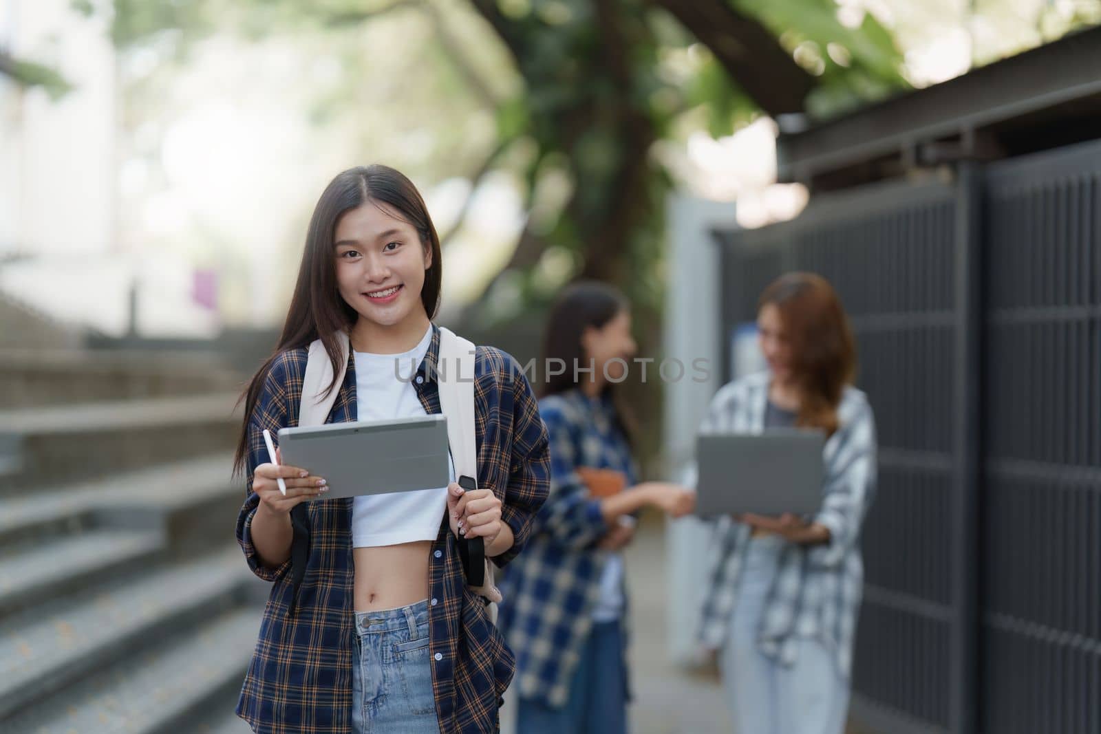 Beautiful young Asian woman college student with friends at outdoors. College student working on the college campus.