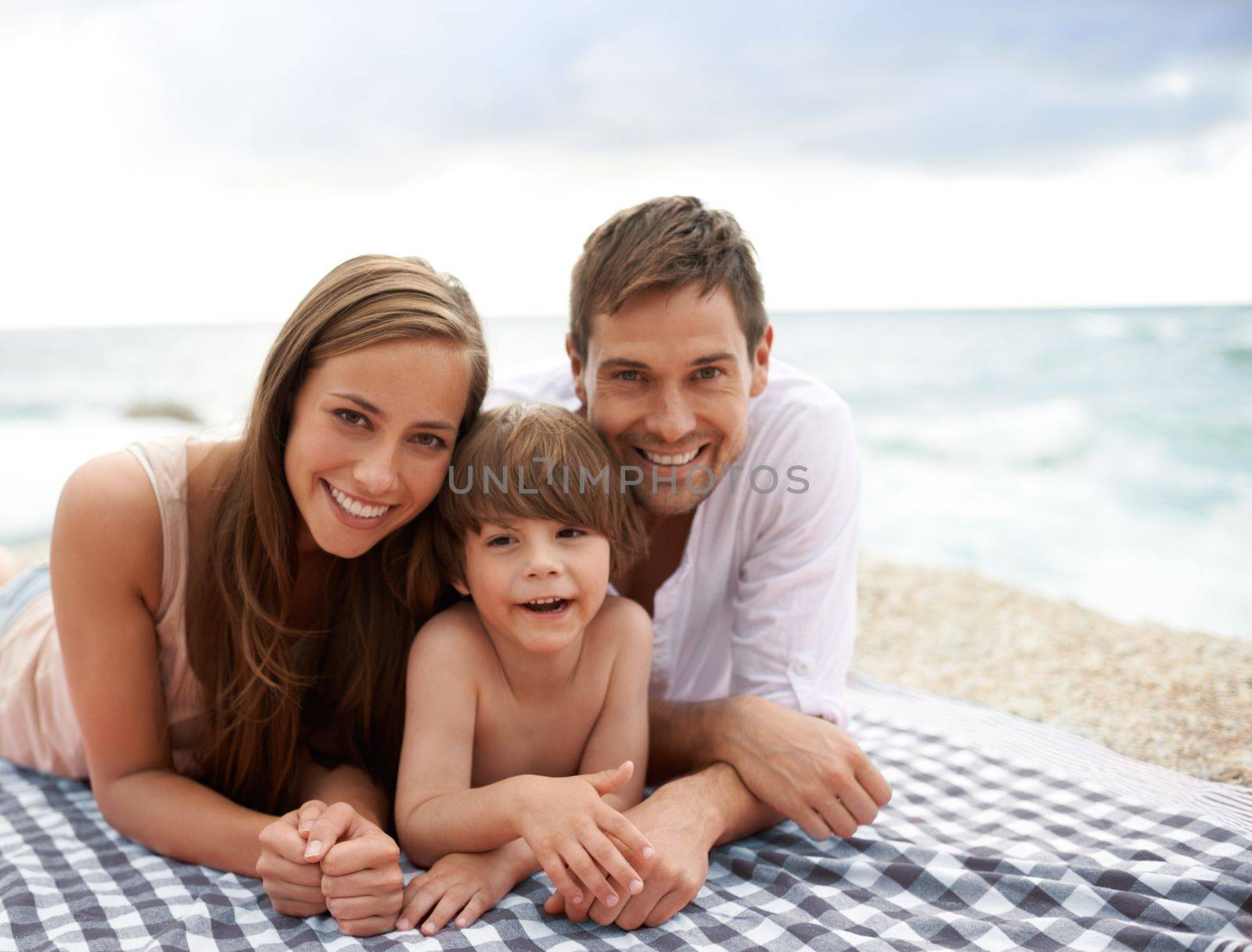 Family fun at the beach. A happy family lying on a beach blanket. by YuriArcurs