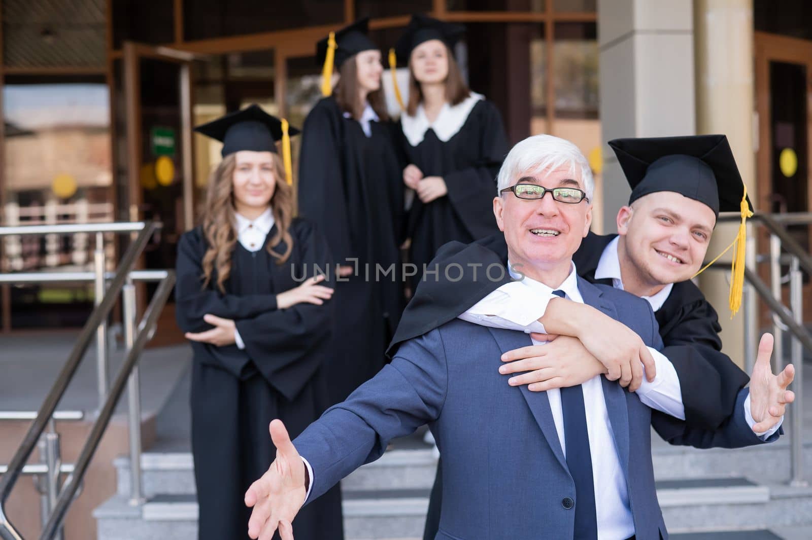 Father and son embrace at graduation. Parent congratulates university graduate. by mrwed54