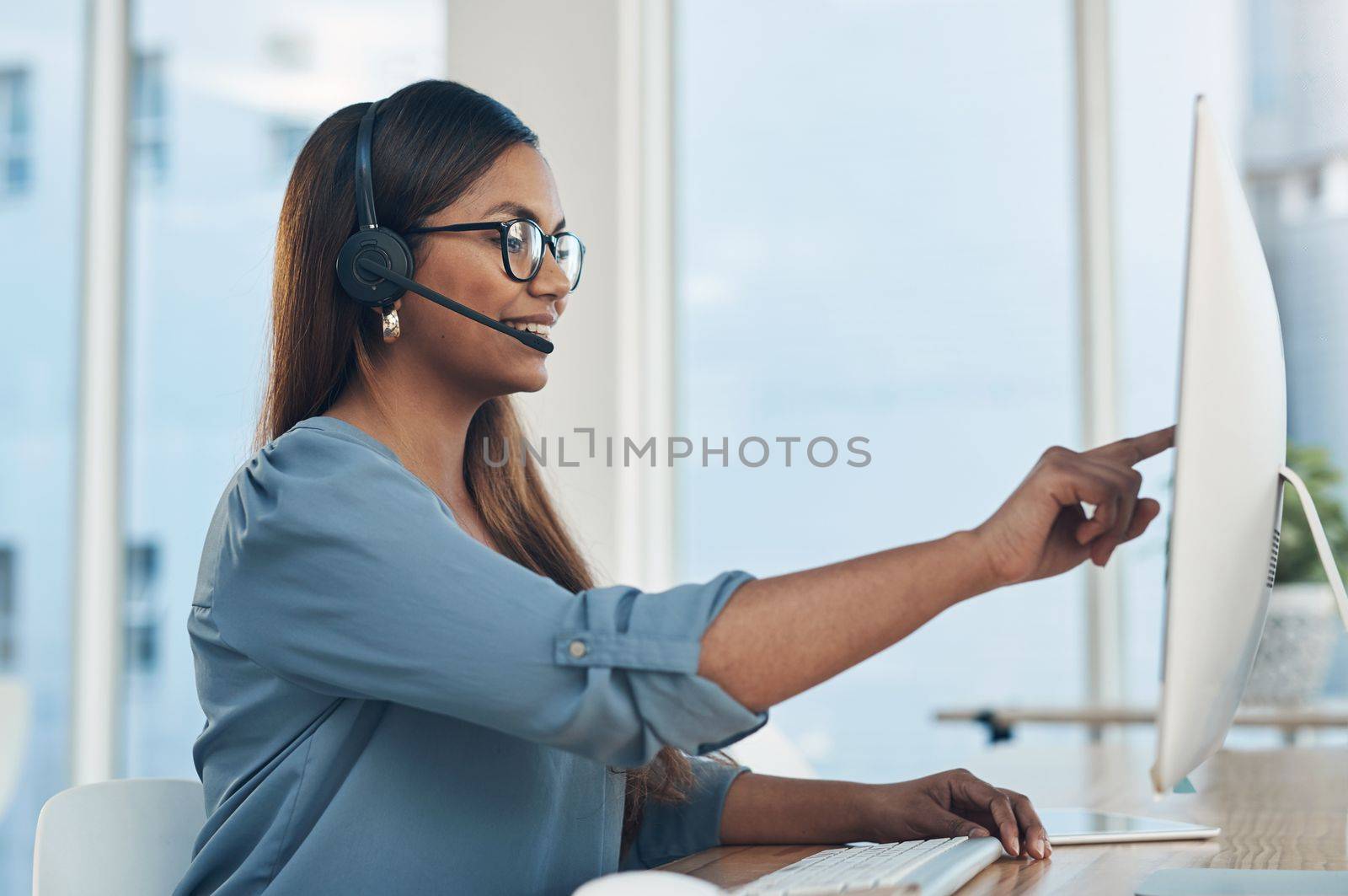 The nature of her work demands good communication skills. a young businesswoman wearing a headset while working on a computer in an office. by YuriArcurs