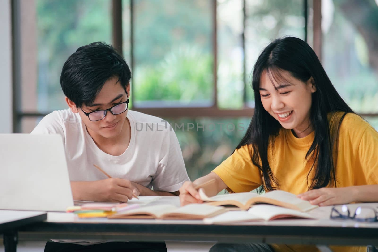 Young asian university students are studying for an exam. There are tutor books with friends. They are classmates that try to help each other. They have been tutoring for many hours in the campus.