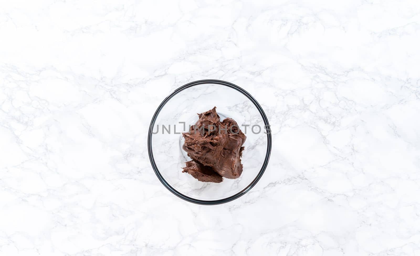 Flat lay. Mixing store-bought chocolate frosting in a mixing glass bowl with a hand mixer.