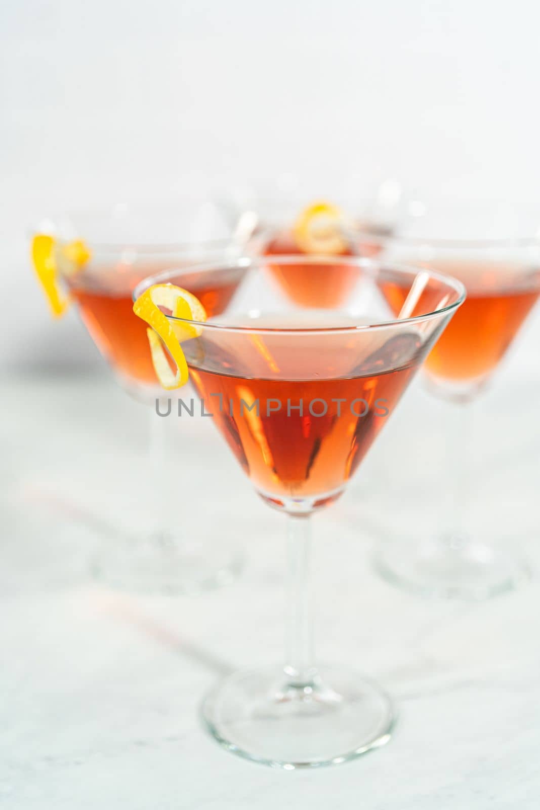 Cosmopolitan cocktail in a martini glass and decorated with a lemon swirl.