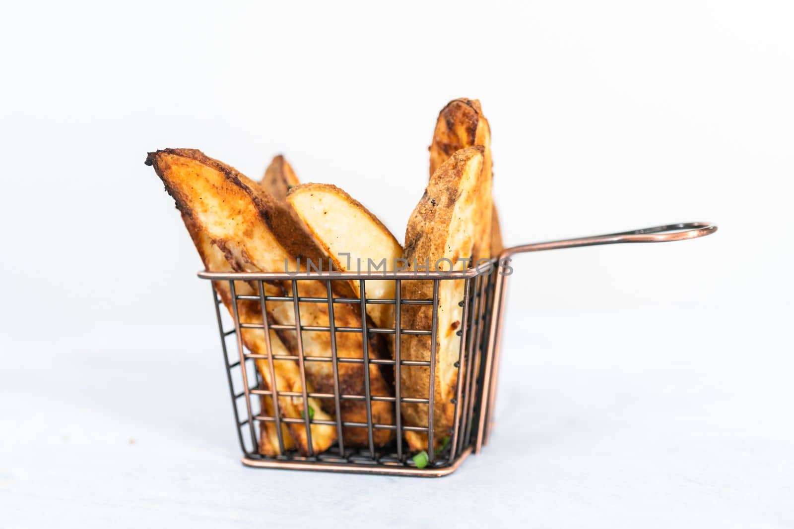 Freshly baked potato wedges with spices in a wire basket.
