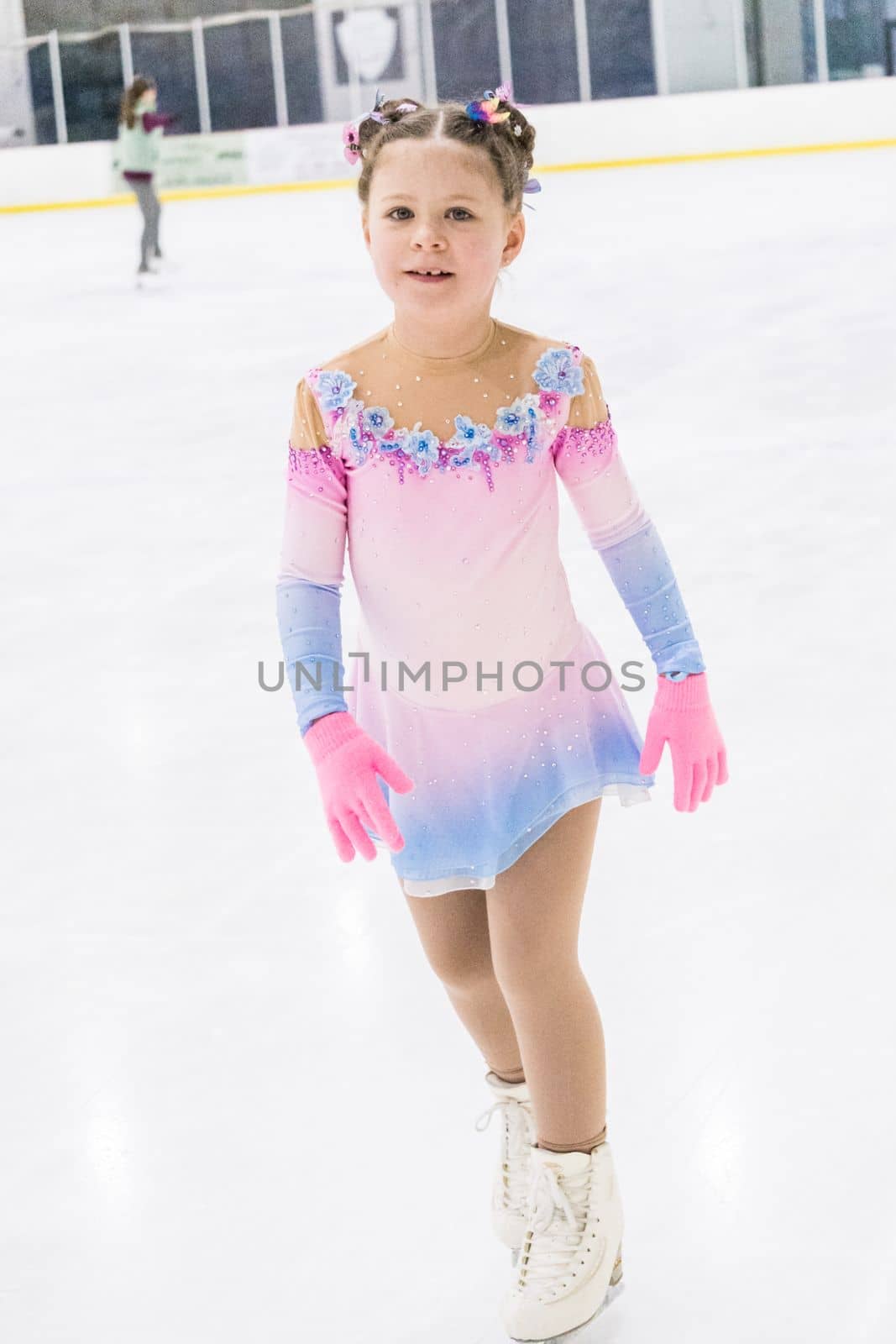 Little girl practicing figure skating on an indoor ice rink.