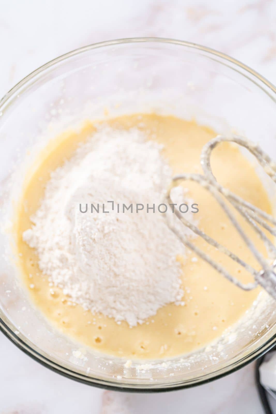 Mixing ingredients in a large glass mixing bowl to bake apple bundt cake with caramel glaze.