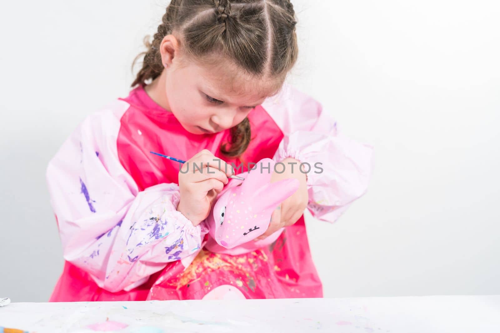 Homeschooling during COVID-19 lockdown. Little girl painting paper mache Easter bunny figurine with acrylic paint.