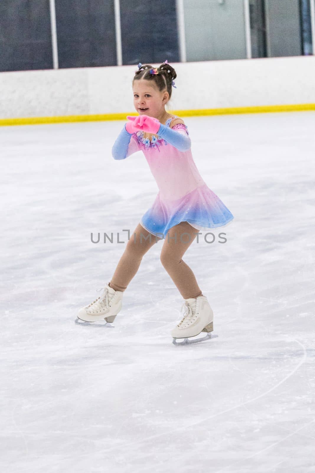 Little girl practicing figure skating on an indoor ice rink.