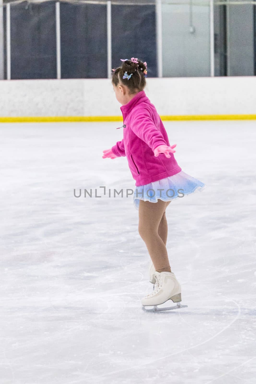 Little girl practicing figure skating on an indoor ice rink.