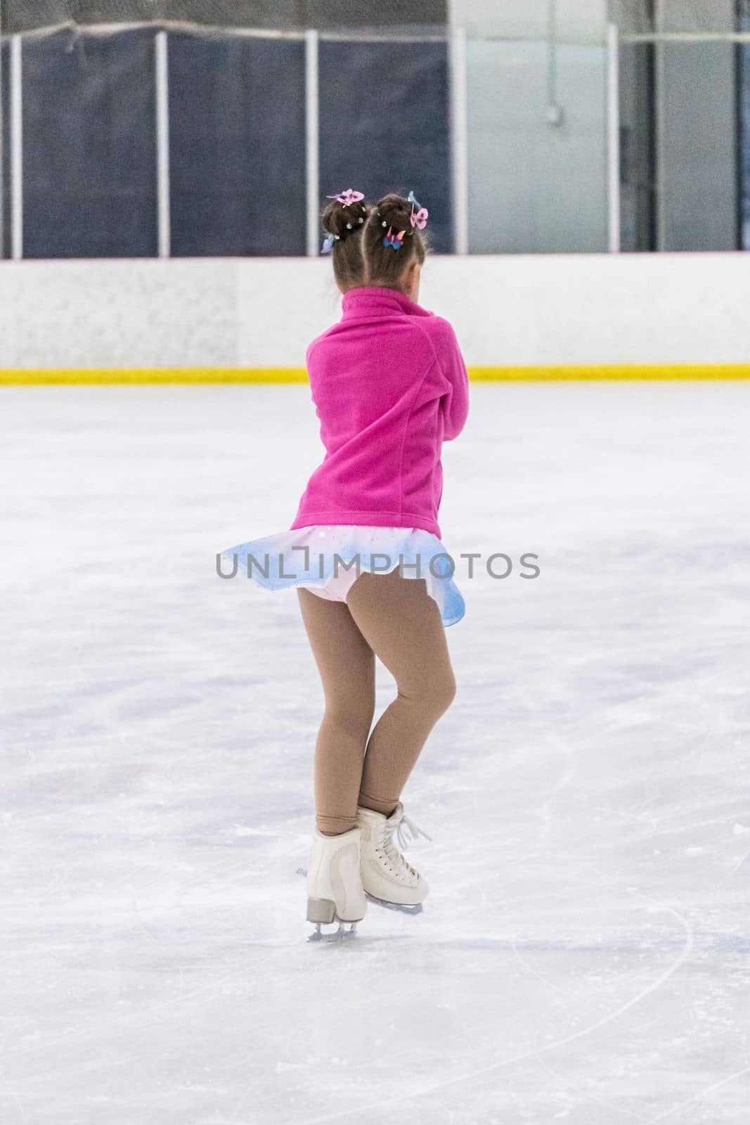 Little girl practicing figure skating on an indoor ice rink.