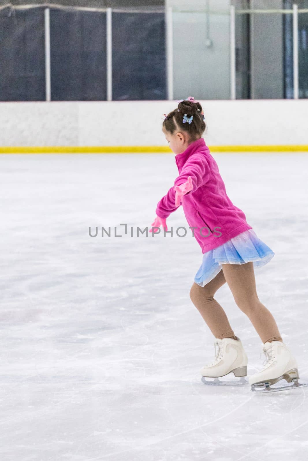 Little girl practicing figure skating on an indoor ice rink.