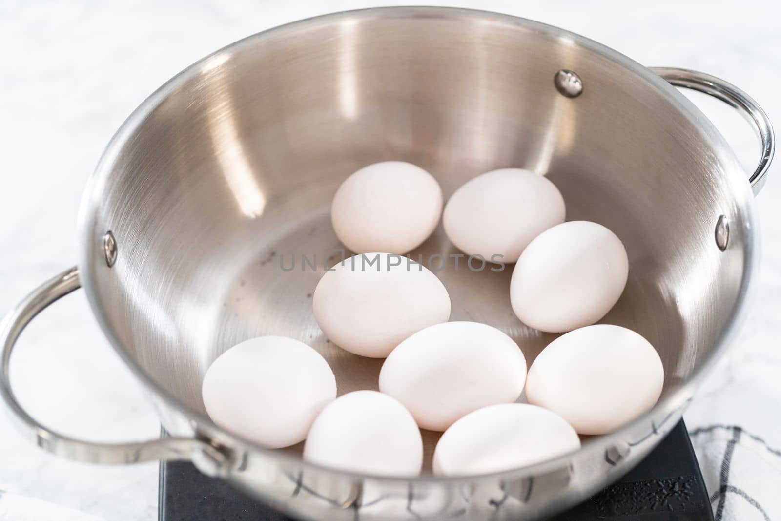 Boiling white eggs in a cooking pot to prepare hard-boiled eggs.