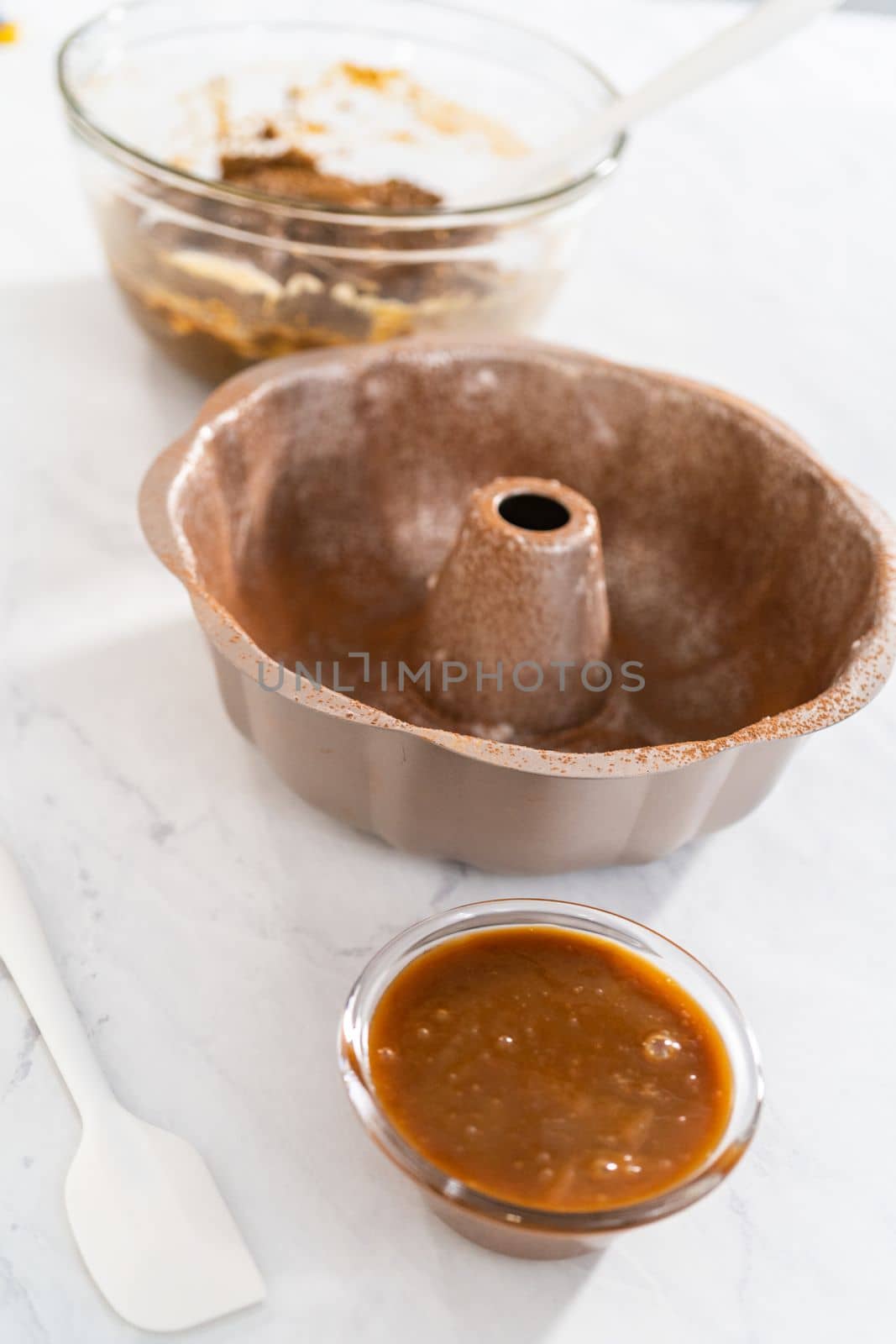 Filling metal bundt cake pan with cake butter to bake gingerbread bundt cake with caramel filling.