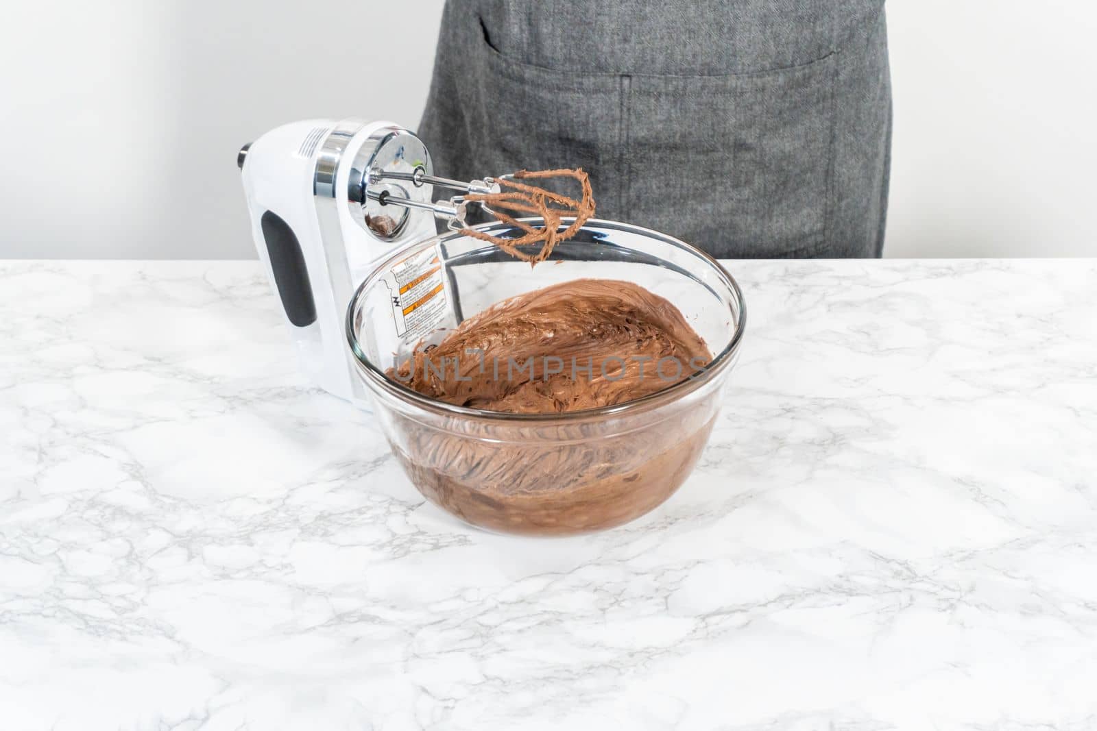 Mixing store-bought chocolate frosting in a mixing glass bowl with a hand mixer.