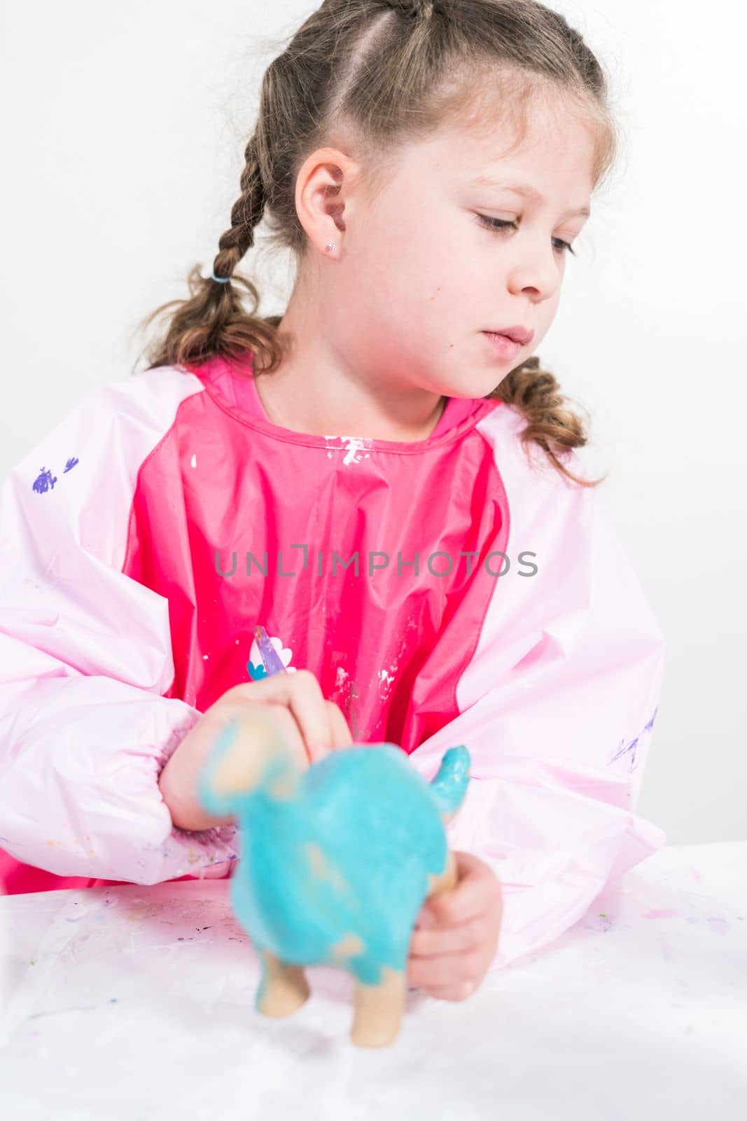 Homeschooling during COVID-19 lockdown. Little girl painting paper mache dinosaur figurine with acrylic paint.