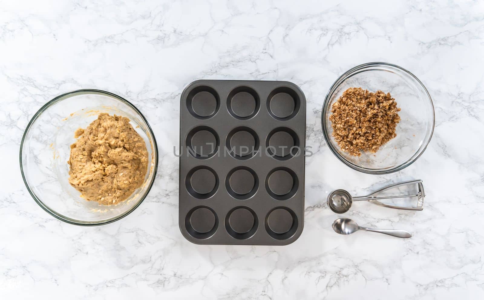 Flat lay. Scooping dough with dough scoop into cupcake pan lined with tulip paper muffin liners to bake banana oatmeal muffins.
