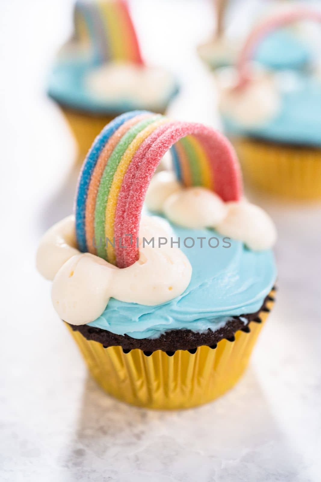 Chocolate cupcakes decorated with blue buttercream frosting and rainbow for unicorn theme birthday party.