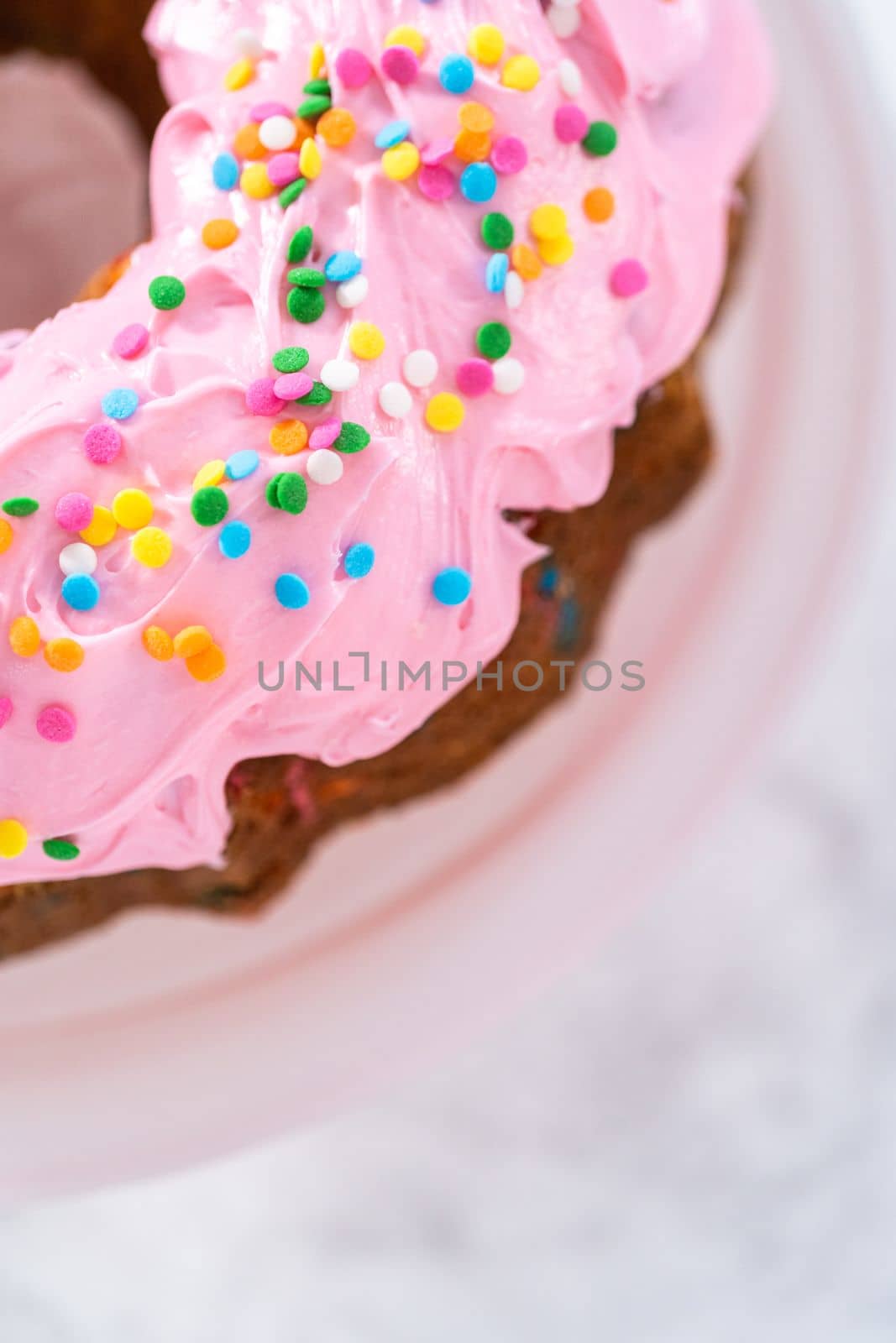 Funfettti bundt cake frosted with pink vanilla buttercream frosting and decorated with rainbow sprinkles.