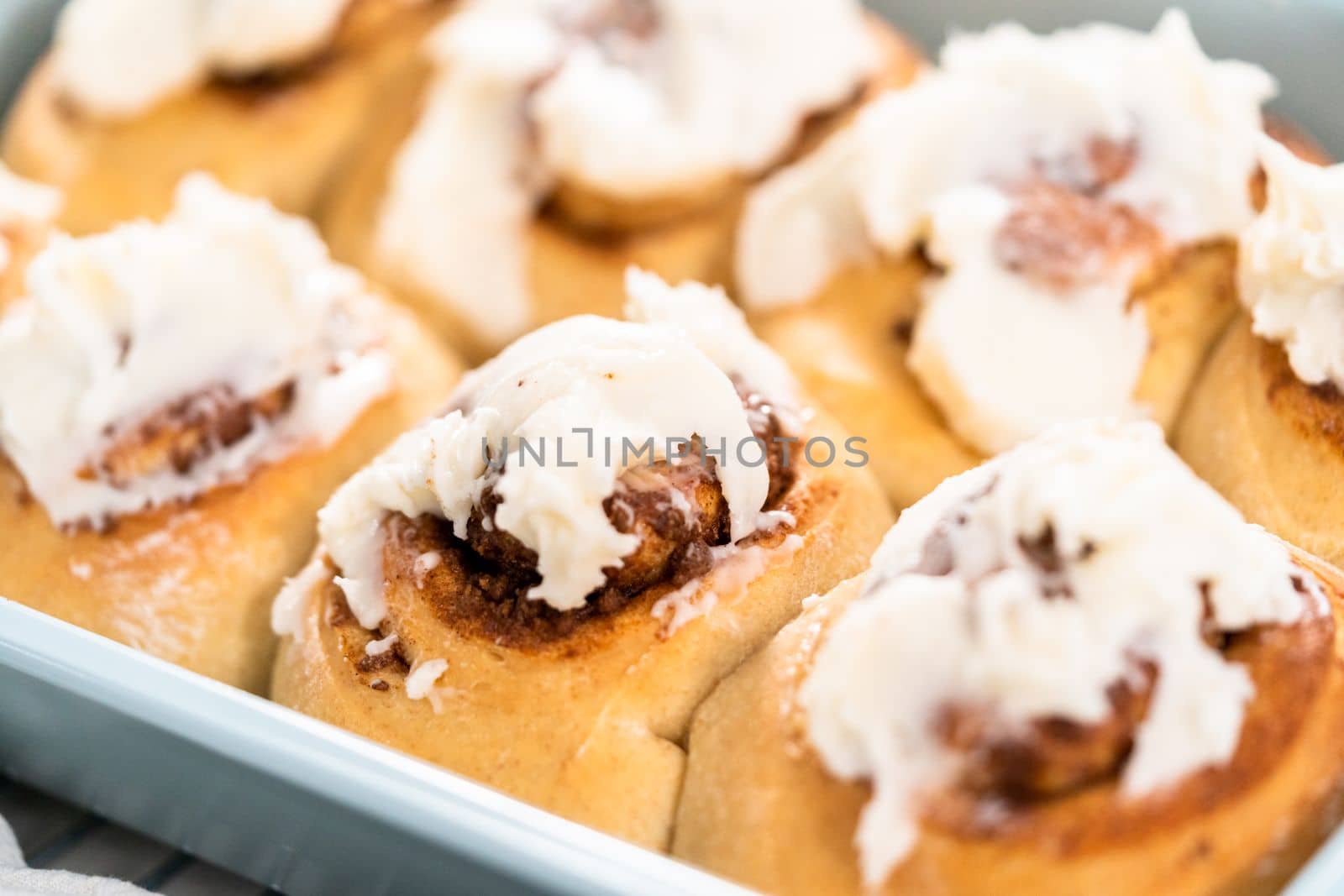 Freshly baked cinnamon rolls with white icing in a blue baking pan.