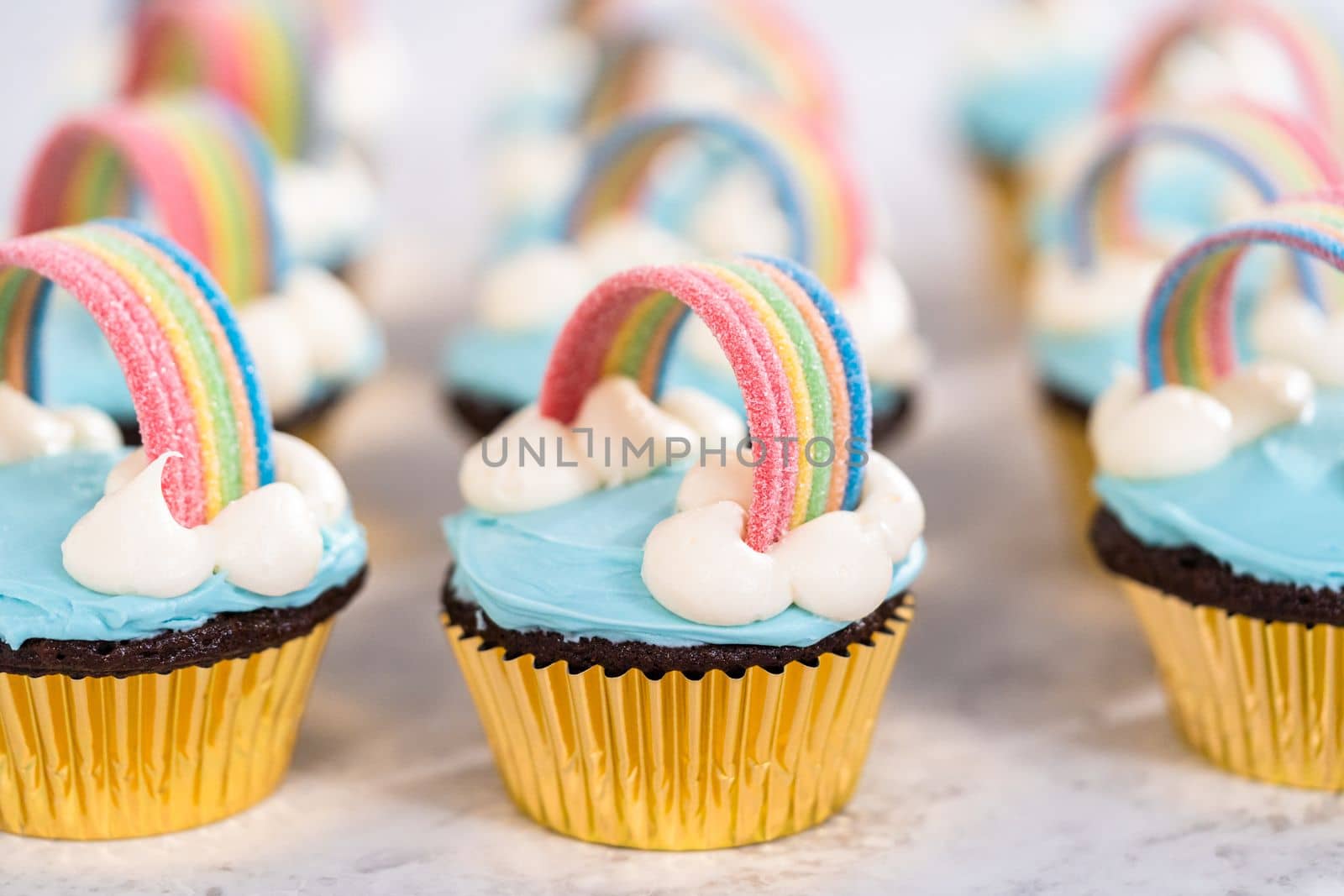 Chocolate cupcakes decorated with blue buttercream frosting and rainbow for unicorn theme birthday party.