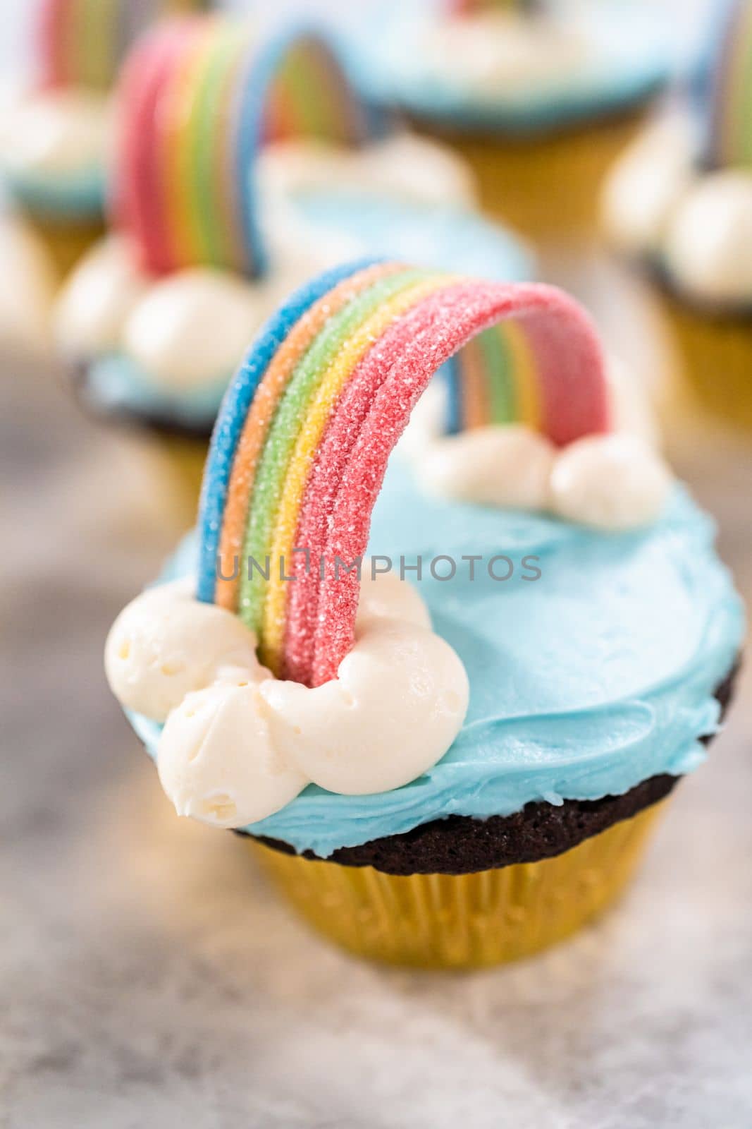 Chocolate cupcakes decorated with blue buttercream frosting and rainbow for unicorn theme birthday party.