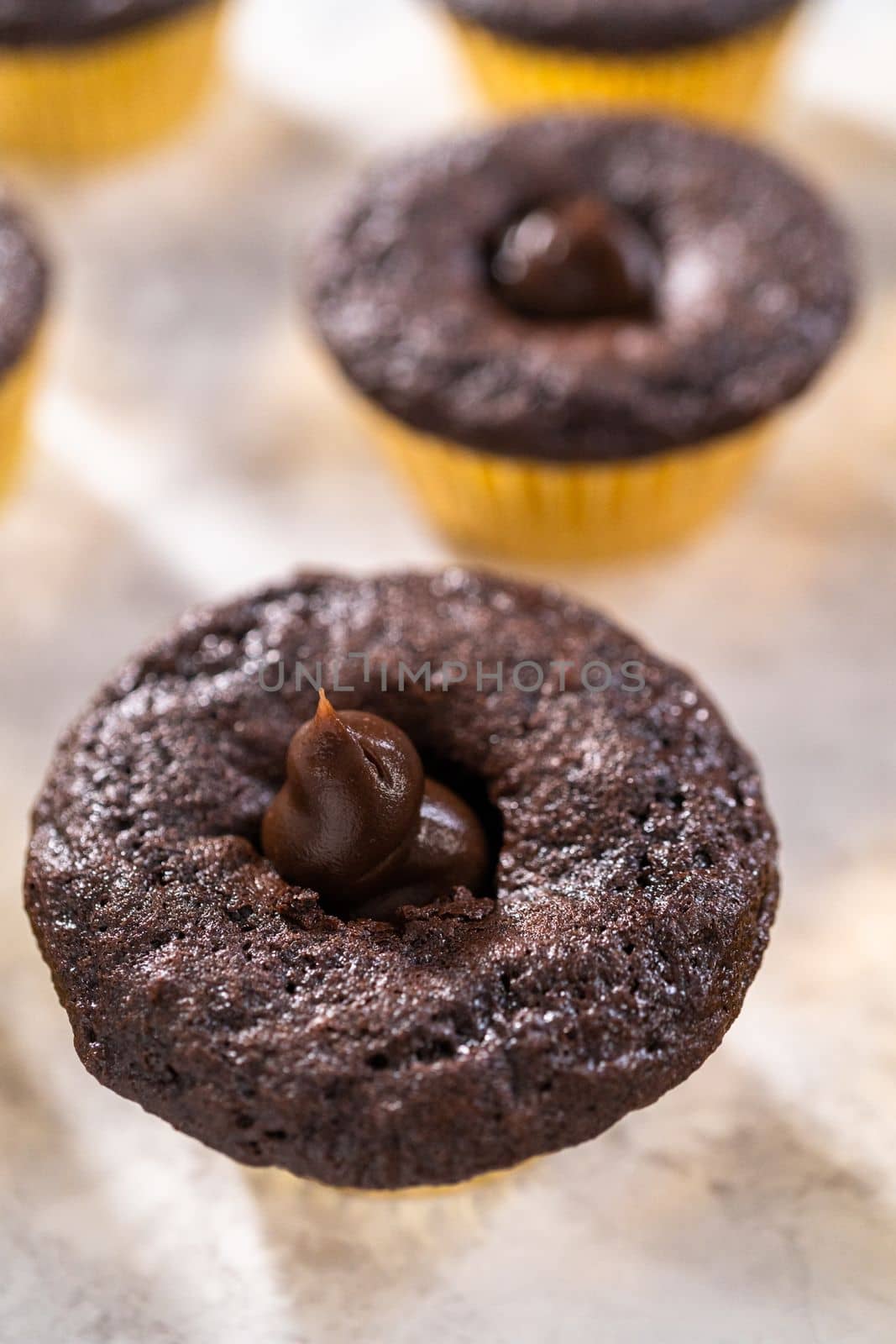 Filling in chocolate cupcakes with chocolate ganache.