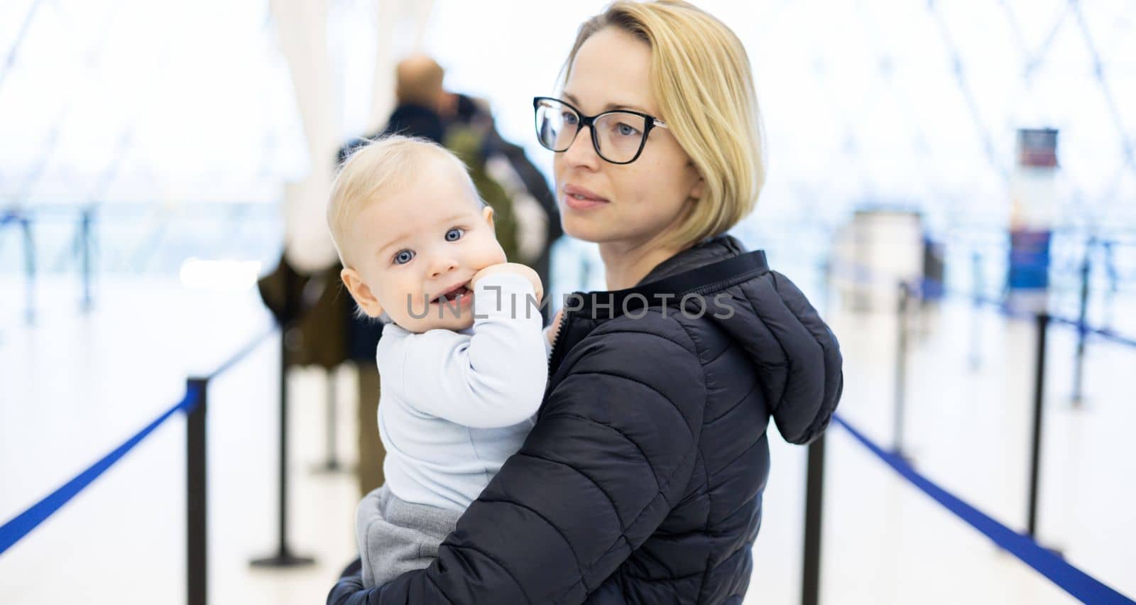 Mother holding his infant baby boy child queuing at airport terminal in passport control line at immigrations departure before moving to boarding gates to board an airplane. Travel with baby concept.