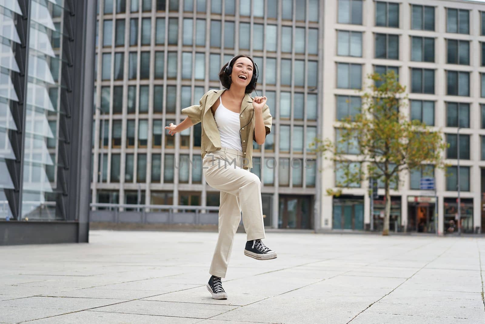 Happy people in city. Upbeat young girl dancing on street in headphones, listening music in headphones.