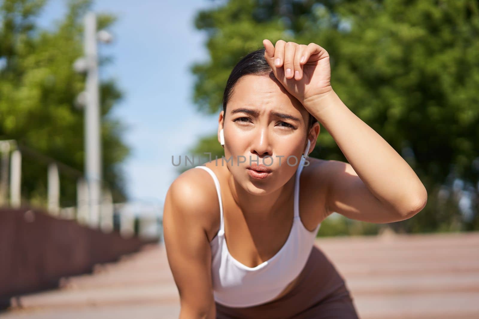 Portrait of asian woman taking break, breathing heavily and panting after running, jogger standing and wiping sweat off forehead, smiling pleased by Benzoix