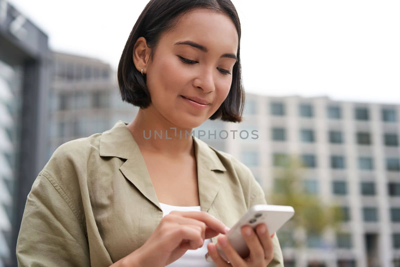 Mobile technology. Smiling asian woman using smartphone app, looking at her telephone on street, checking map, calling or texting someone by Benzoix