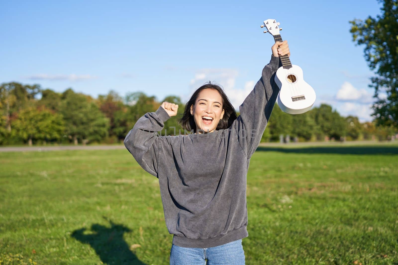 Positive beauty girl with ukulele, dancing and feeling freedom, looking excited, triumphing and celebrating.
