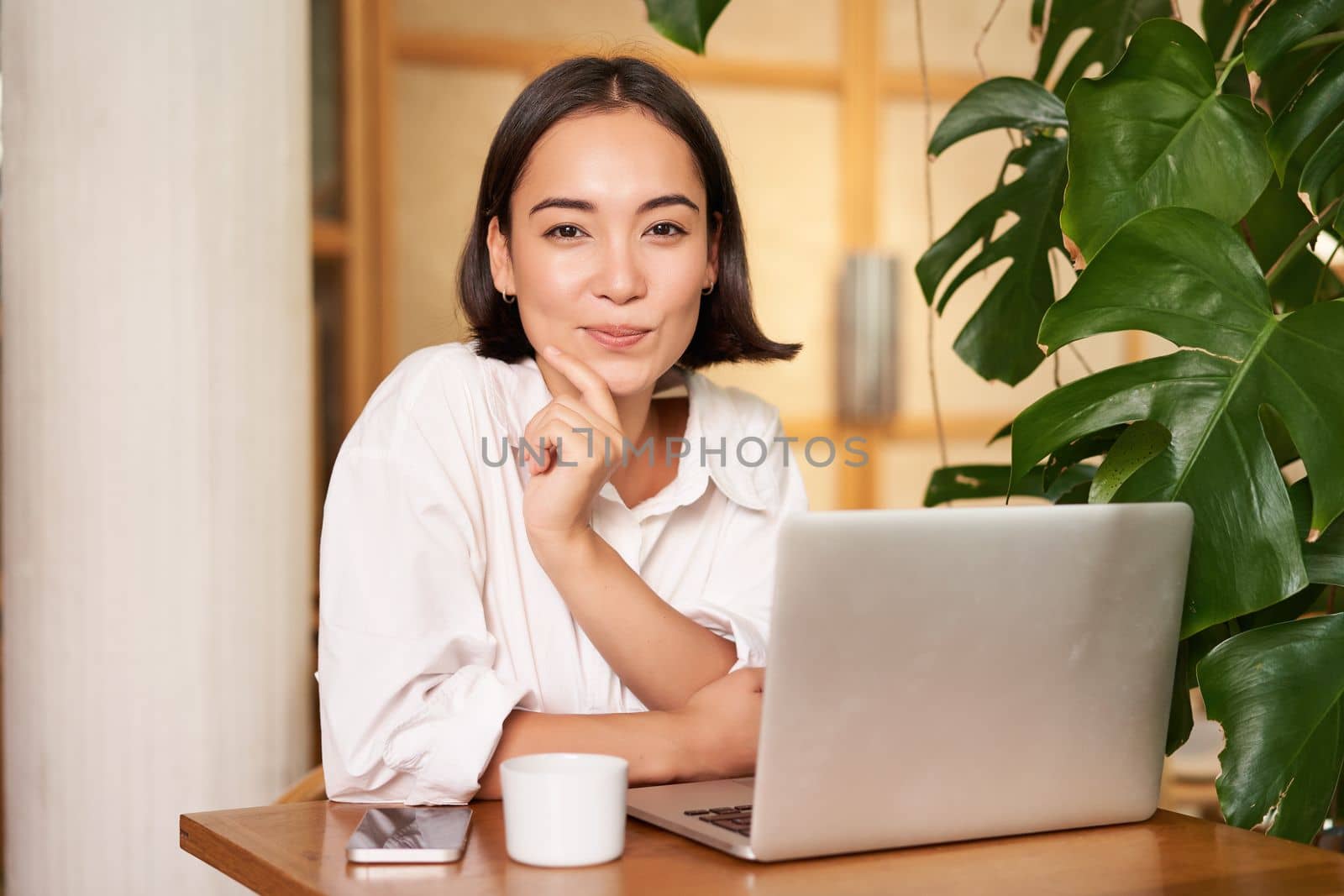 Confident young stylish woman with laptop, sitting in cafe and working, freelancer in co-working space with cup of coffee.