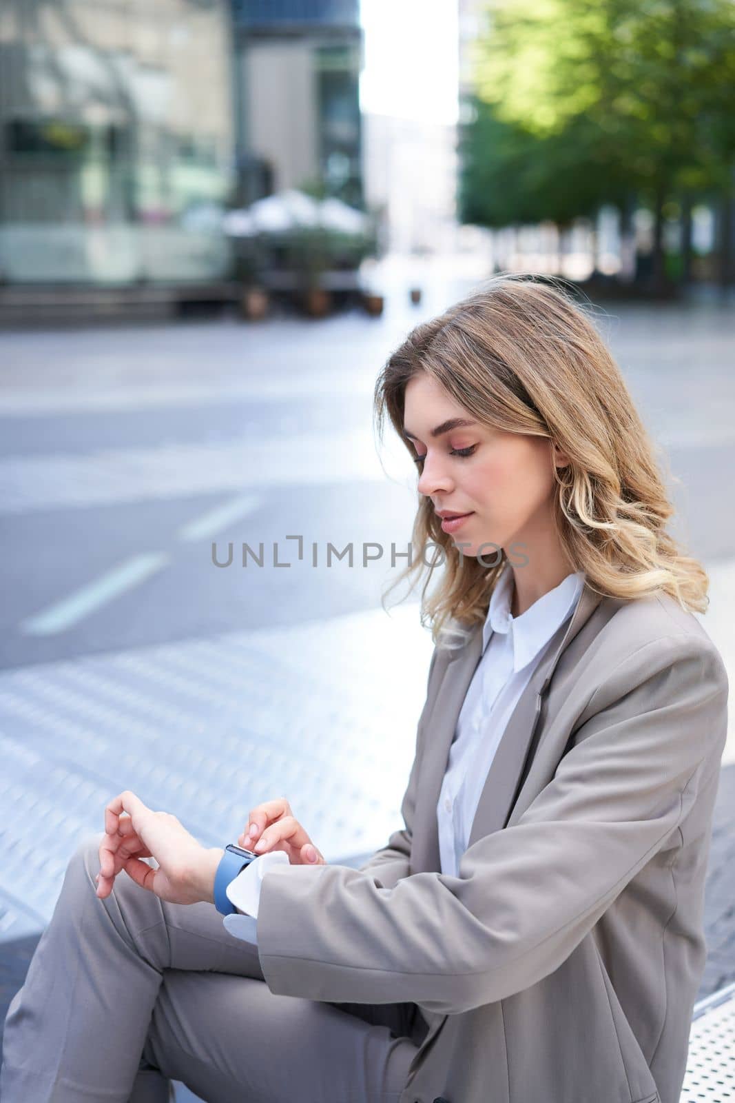 Vertical shot of businesswoman looking at time on her watch, waiting for coworker, having a business meeting outdoors.