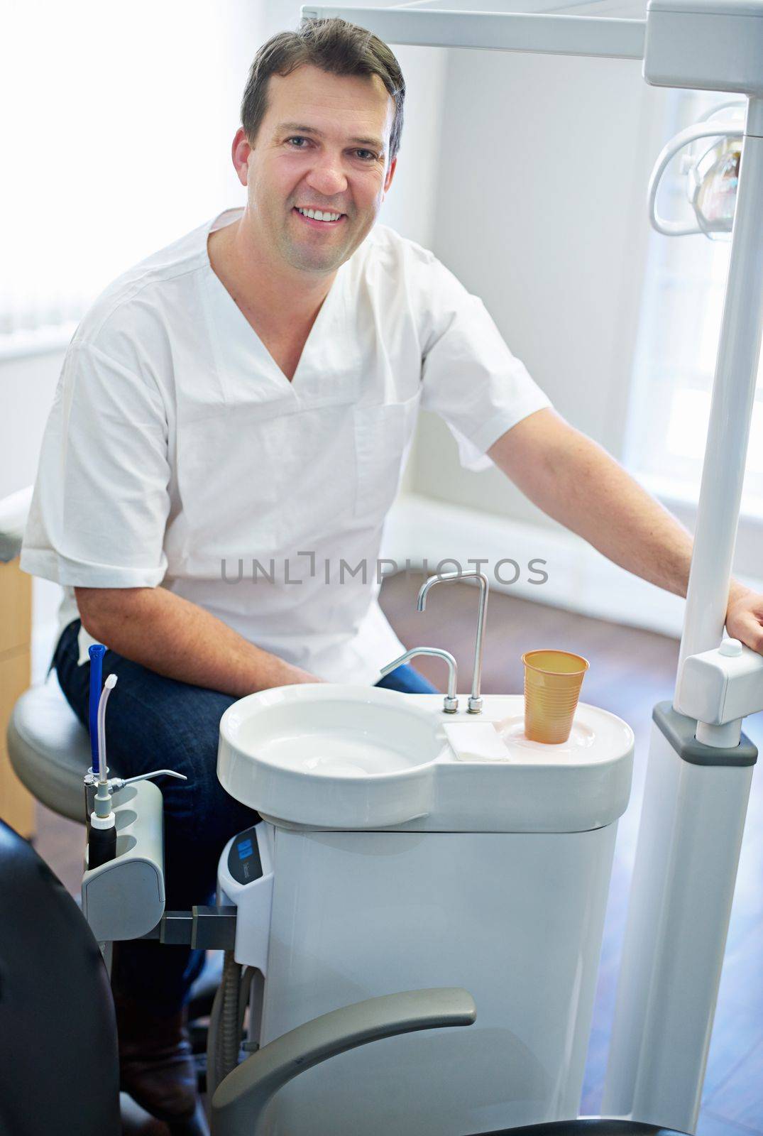 I hope youve been brushing. Portrait of a male dentist sitting by the dental equipment in his office. by YuriArcurs