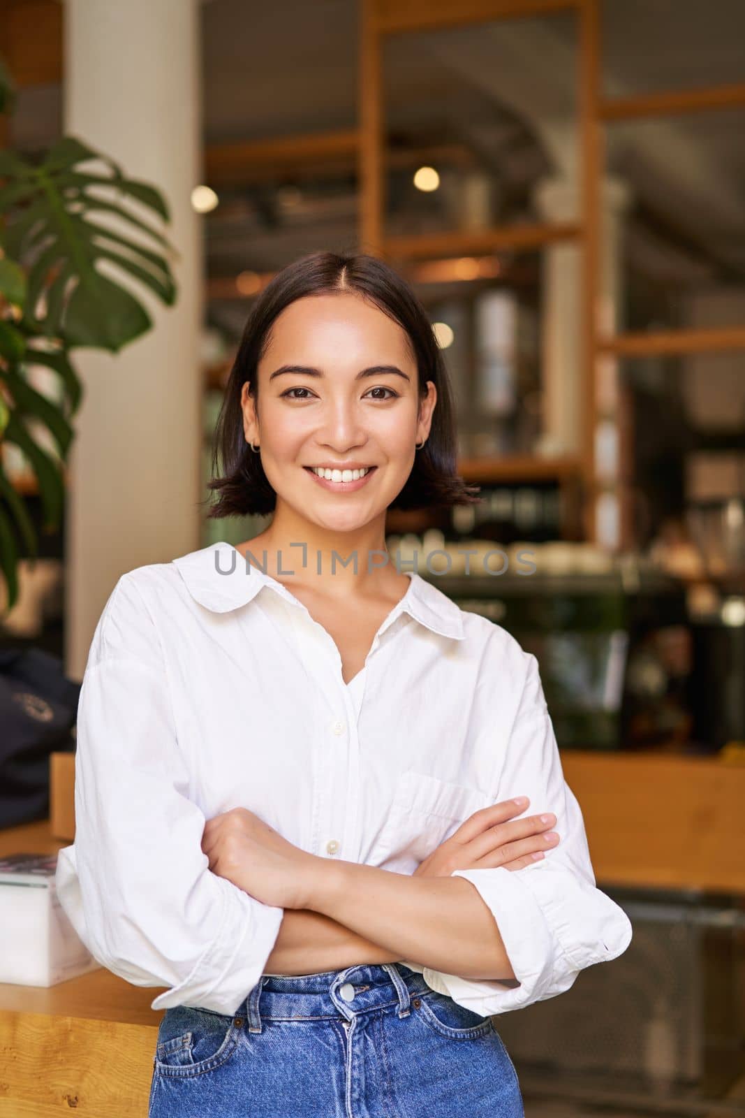 Portrait of young female entrepreneur, cafe owner, standing at the door entrance and smiling, looking confident.