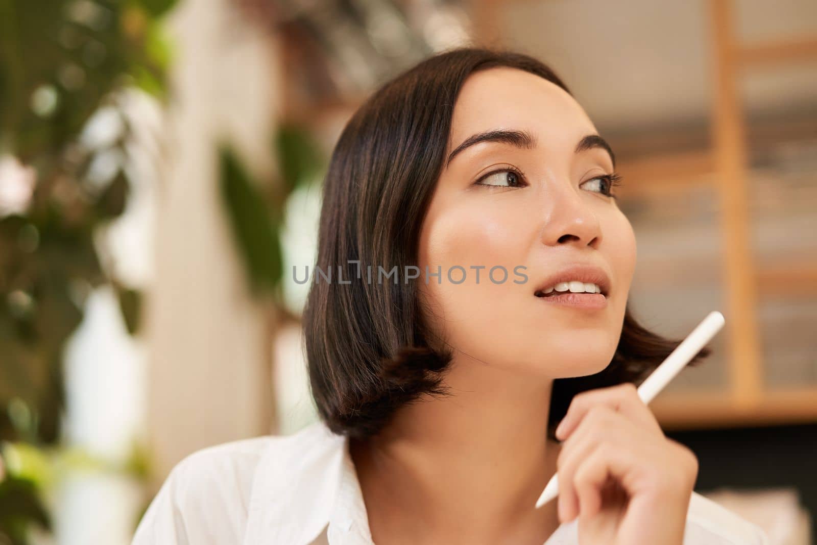 Close up portrait of stylish young brunette woman, sitting with graphic pen and smiling, relaxing in cafe, writing something, making notes.