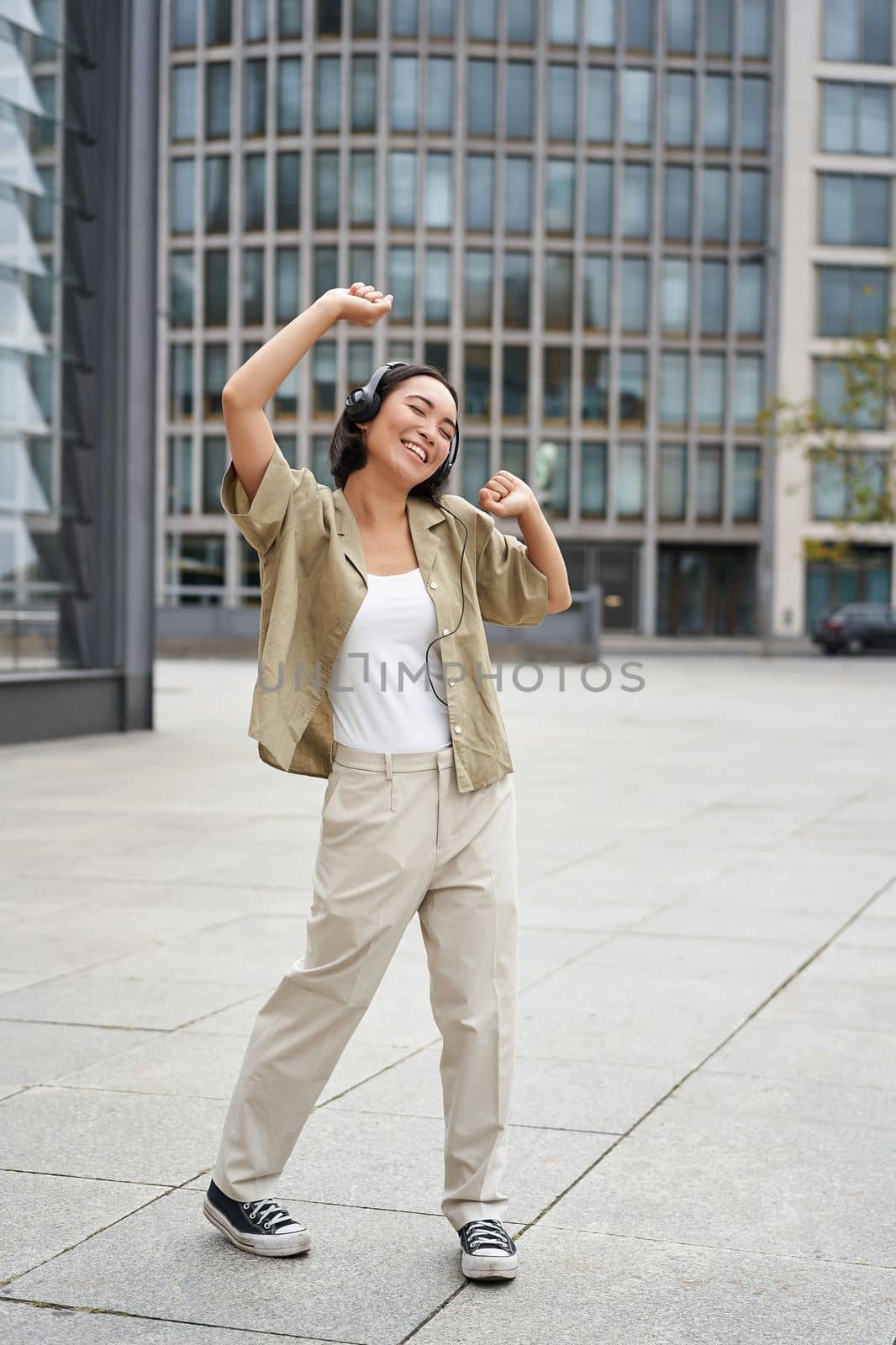 Girl dances on street with headphones on, listens to music and feels happy walking in city.