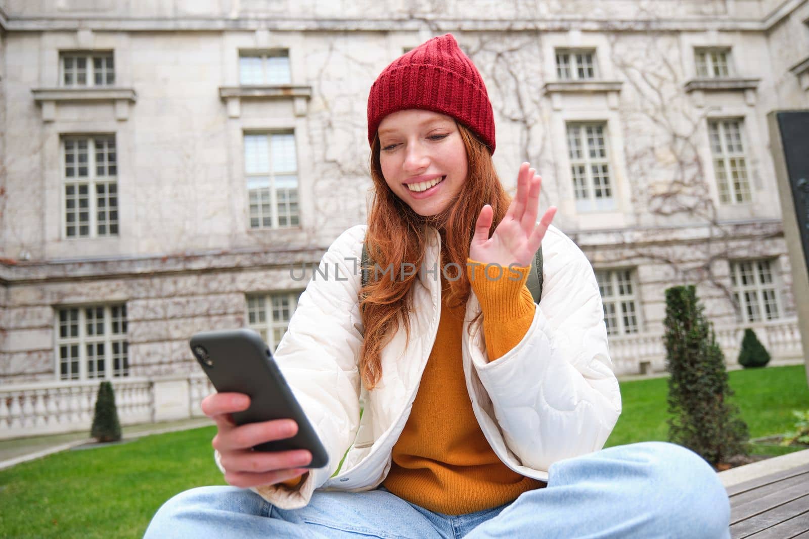 Smiling young woman says hello on video chat, connects public wifi in park and talks someone online with smartphone app.