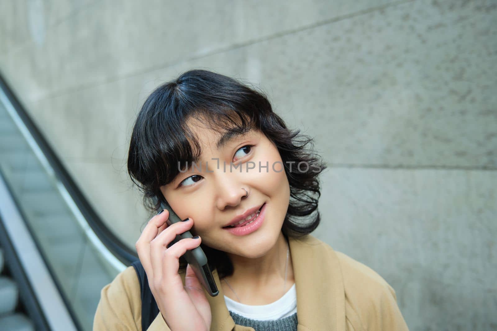 Close up portrait of smiling brunette girl, korean woman goes down escalator, makes phone call, talks to someone on telephone.