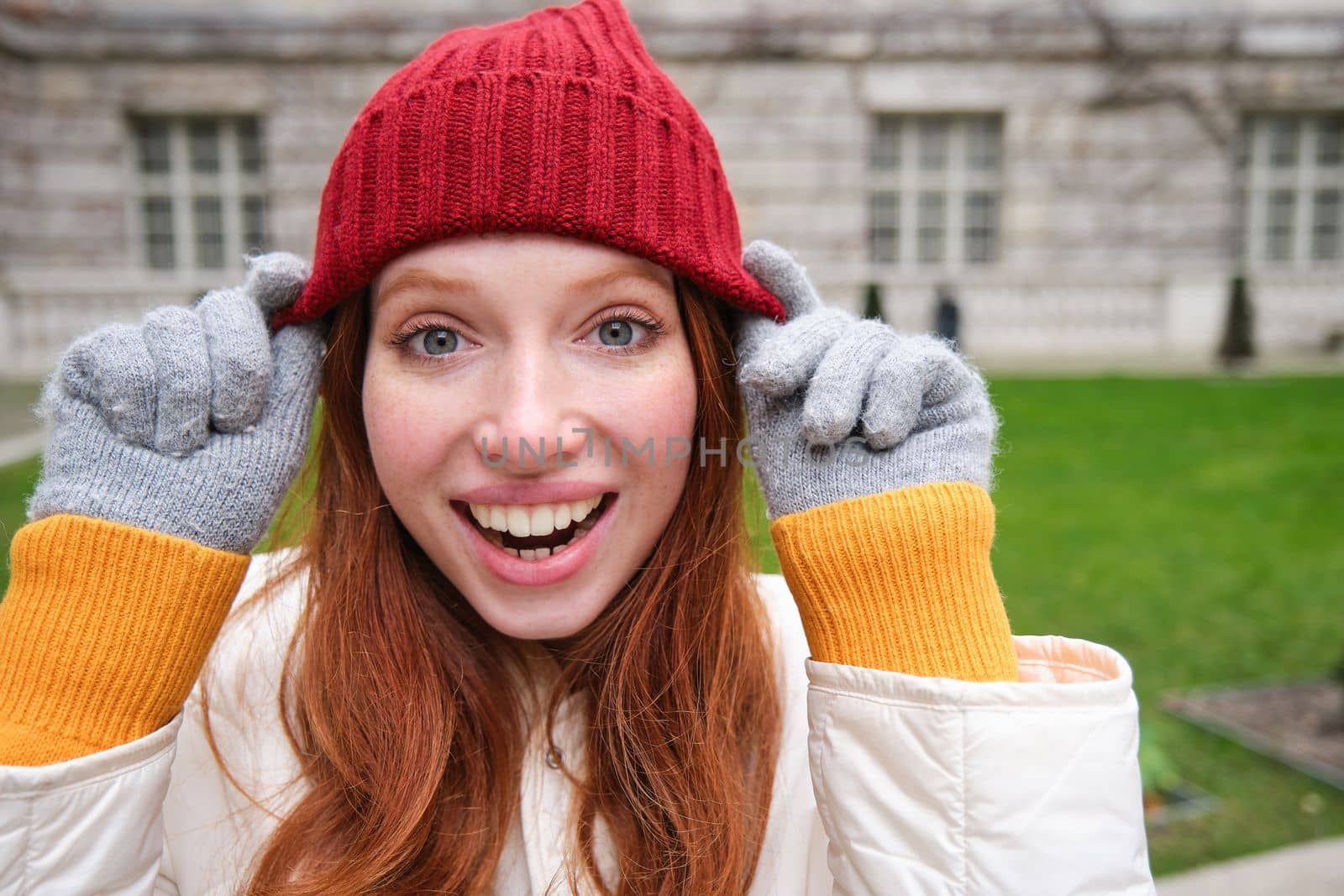 Cute girl student in red hat, warm gloves, sits in park, smiles and looks happy. Copy space