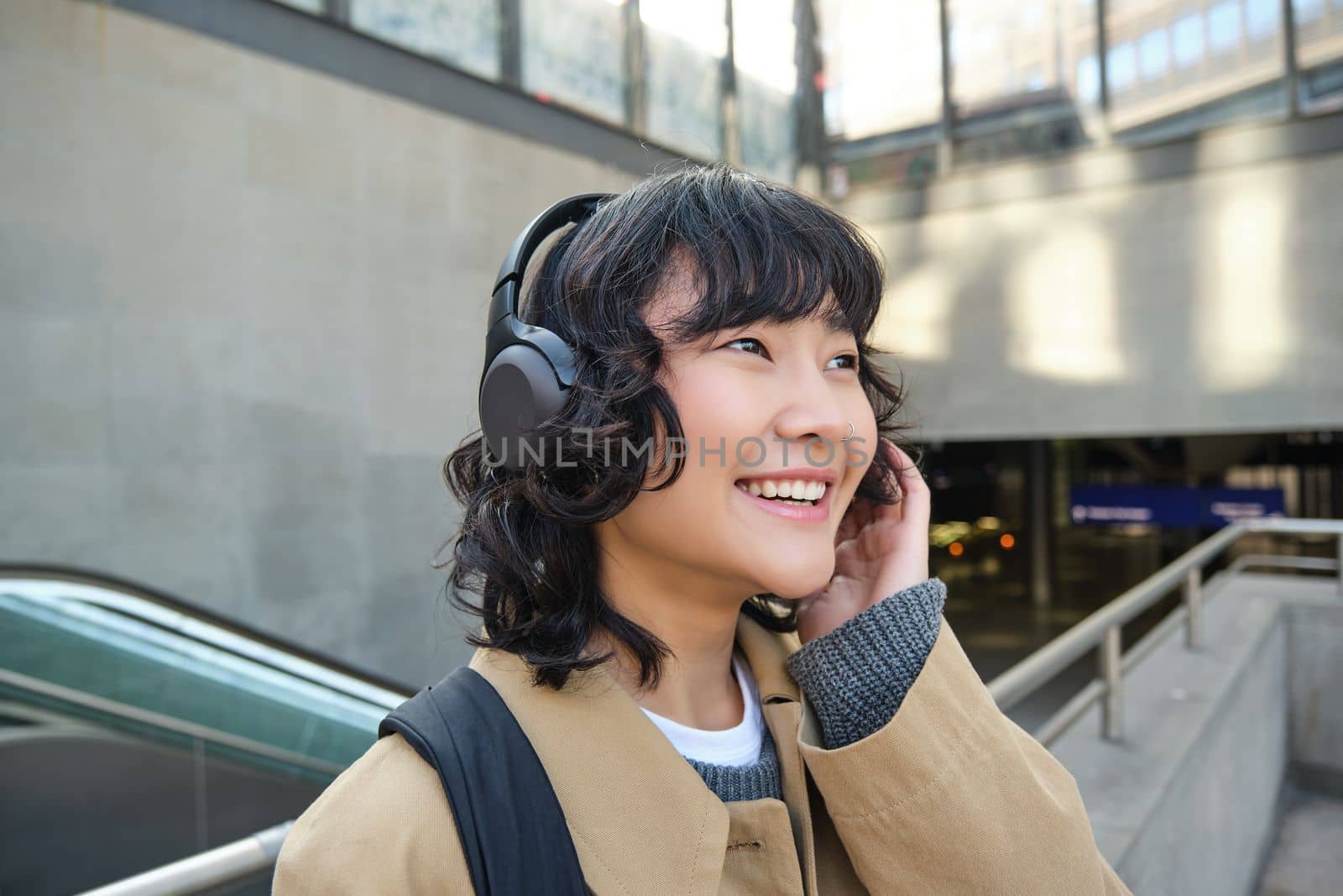 Close up portrait of Korean girl in headphones, student listens music in headphones and smiles, walks around city, tourist travelling.