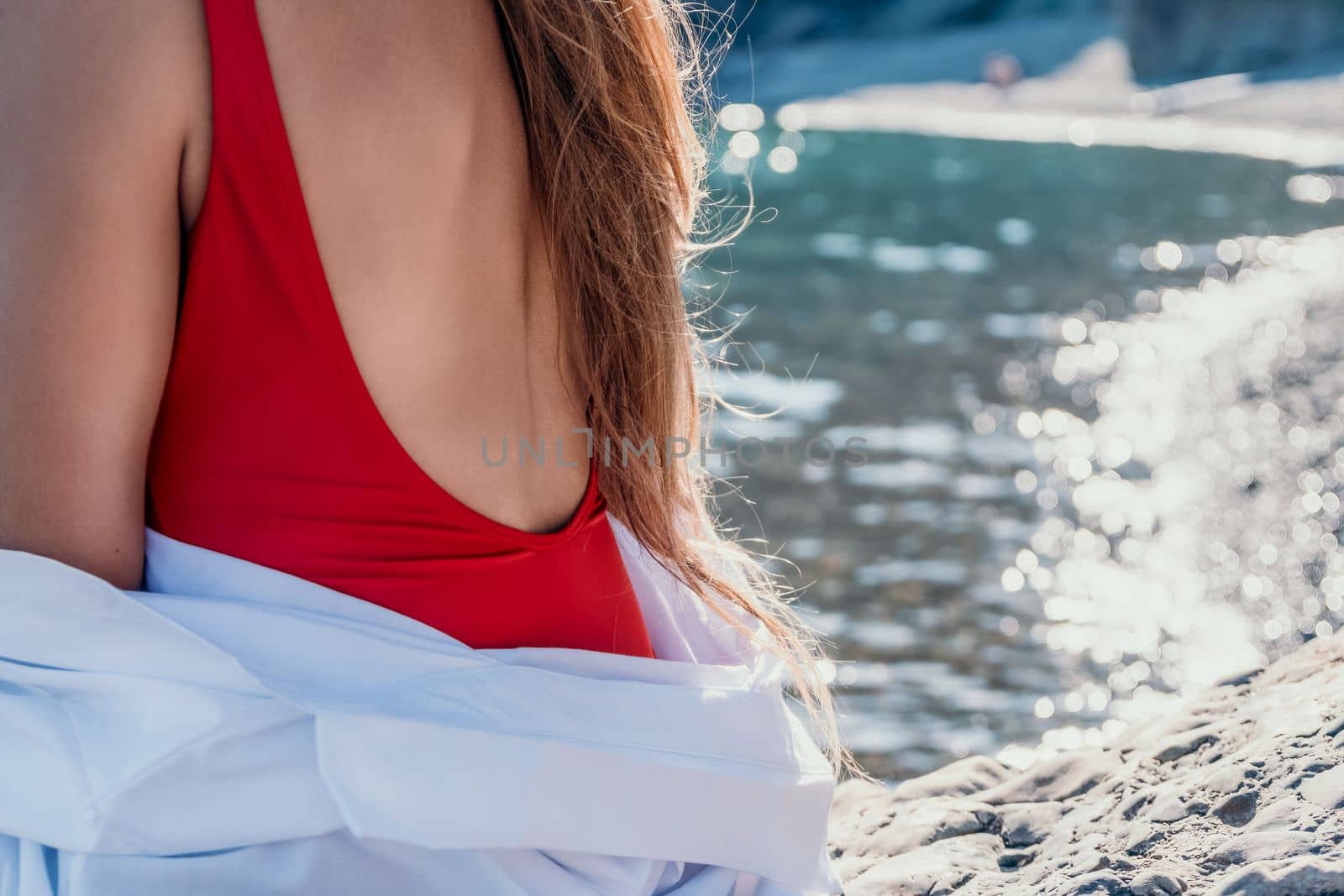 Young woman in red bikini on Beach. Girl lying on pebble beach and enjoying sun. Happy lady in bathing suit chilling and sunbathing by turquoise sea ocean on hot summer day. Close up. Back view by panophotograph